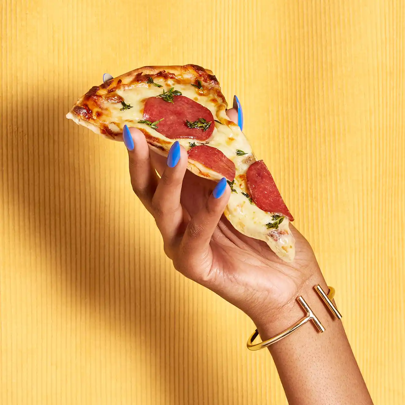 Greasy Glamour Content styled hands with bright finger nails holding slice off pizza in front of velvet background